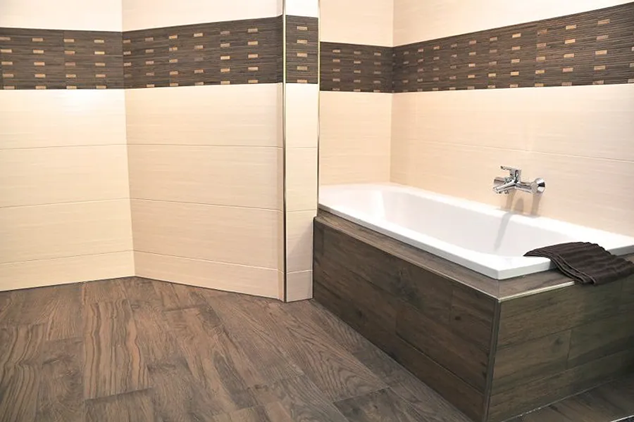 Badewanne mit dunkler Holzoptik-Verkleidung, passendem Fliesenboden und hellen Wandfliesen
